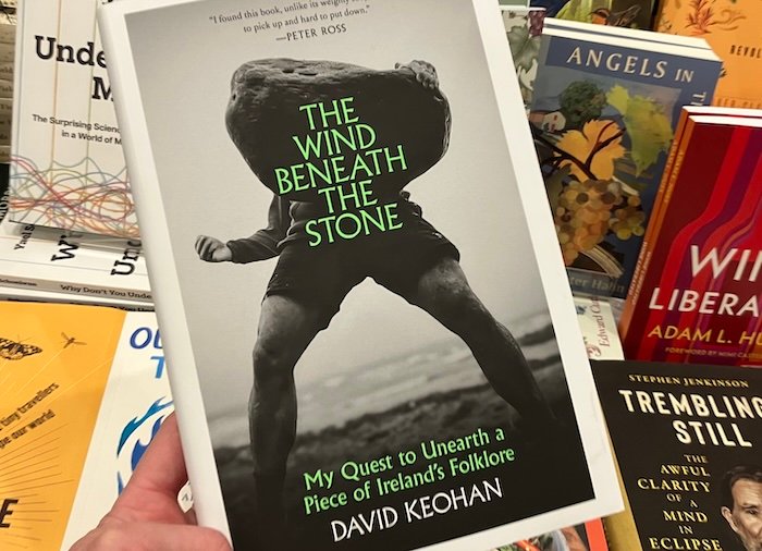 Book Cover image of man holding large stone with green text reading The Wind Beneath the Stone.